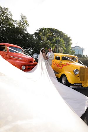 Wedding photo with vintage cars showing long flowing bridal veil against tropical backdrop.