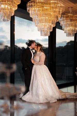 Romantic moment under crystal chandeliers with dramatic window view.