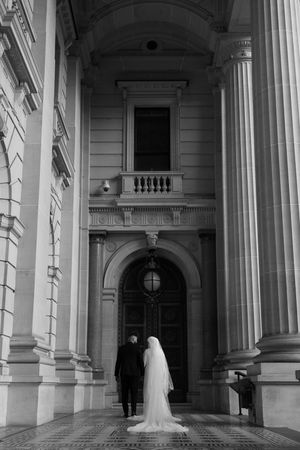Dramatic black and white photo of couple under classical architectural columns and arches.