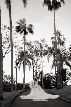 Black and white wedding photo with bride in flowing dress surrounded by palm trees.