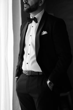 Elegant monochrome photo of groom in classic tuxedo with bowtie by window.