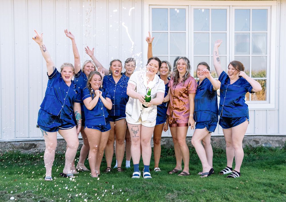 Fun group photo of wedding party sitting and cheering against white building.