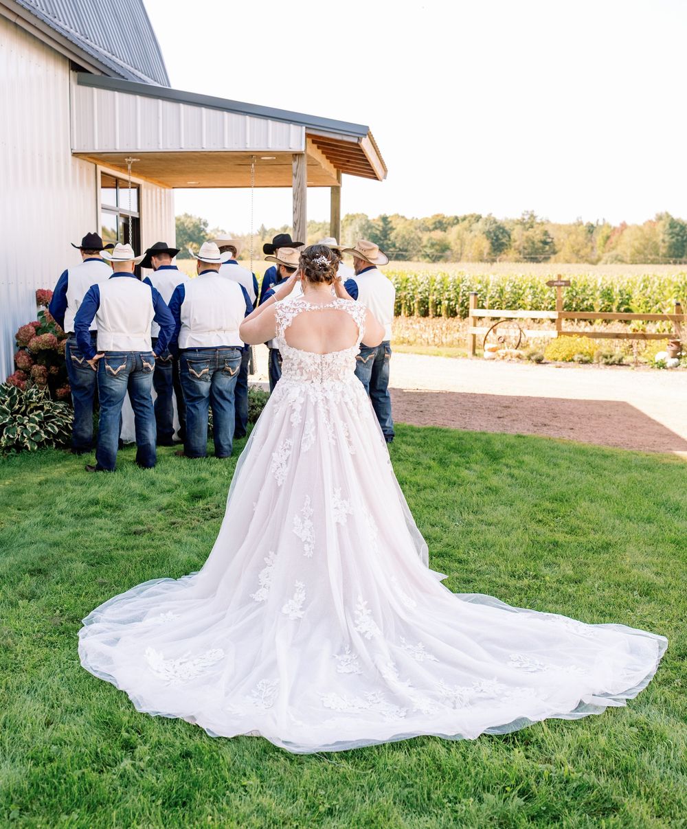 Wedding dress train spread out on grass with guests in background at outdoor venue.