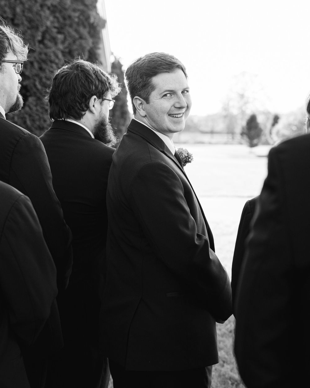 Black and white candid photo of groomsmen chatting before wedding ceremony.
