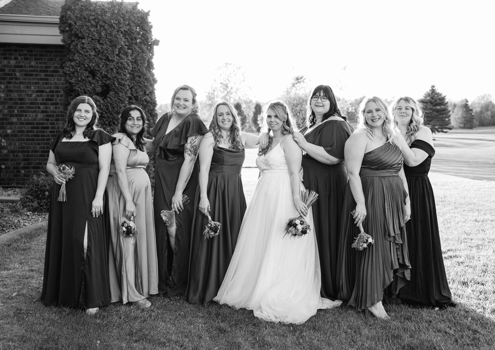 Wedding party in coordinated attire poses for group photo on grounds of historic venue.