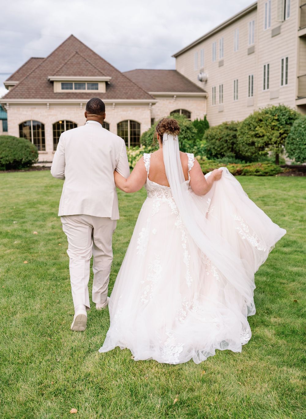 Couple walking on grass path towards elegant building in formal wedding attire.