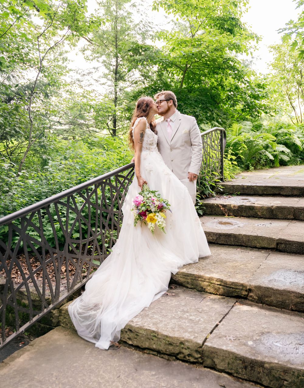 Romantic wedding portraits on stone steps with rustic metal railing in garden setting.