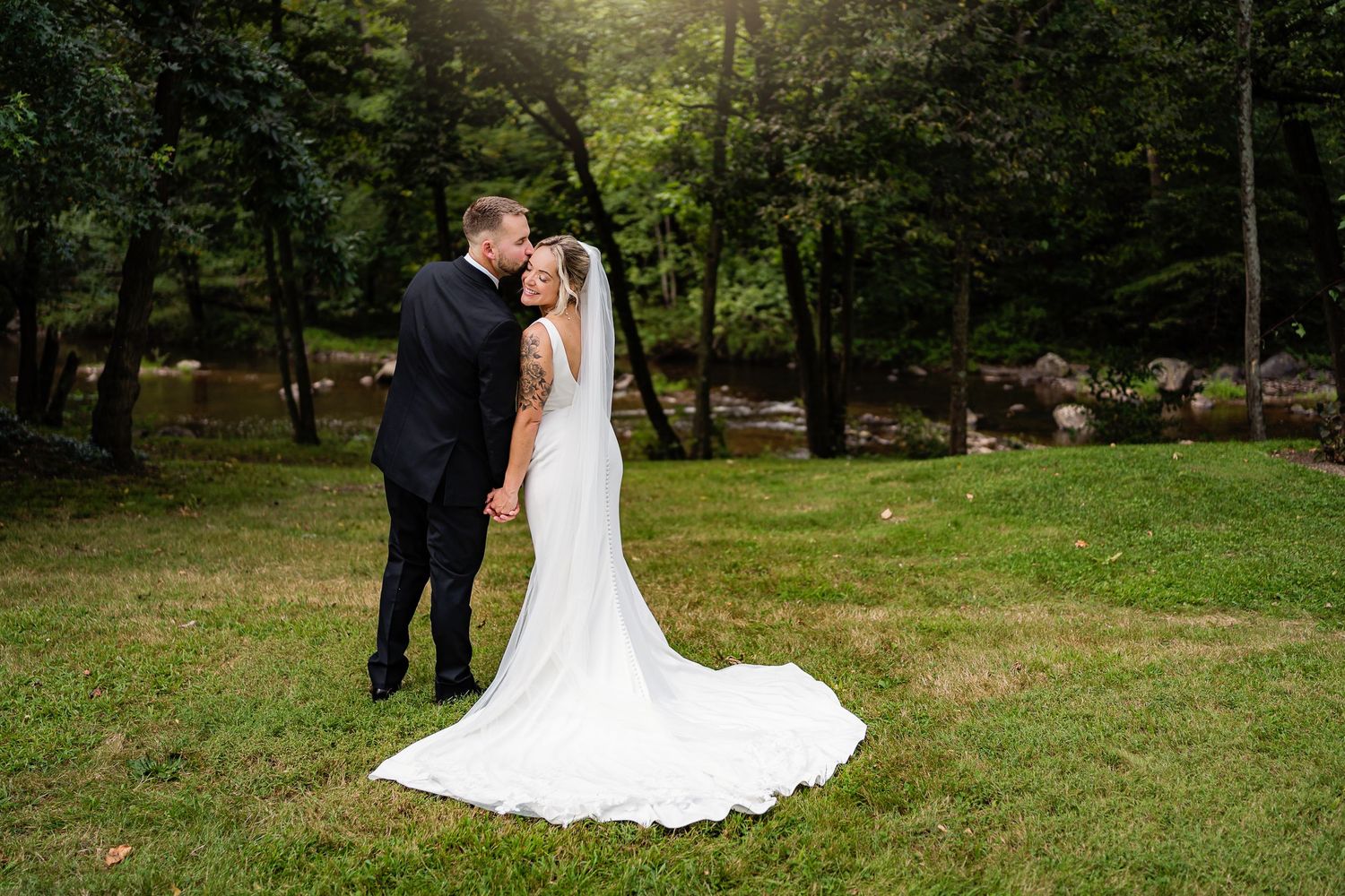 A couple in wedding attire shares a romantic moment in a lush green garden setting during their special day.