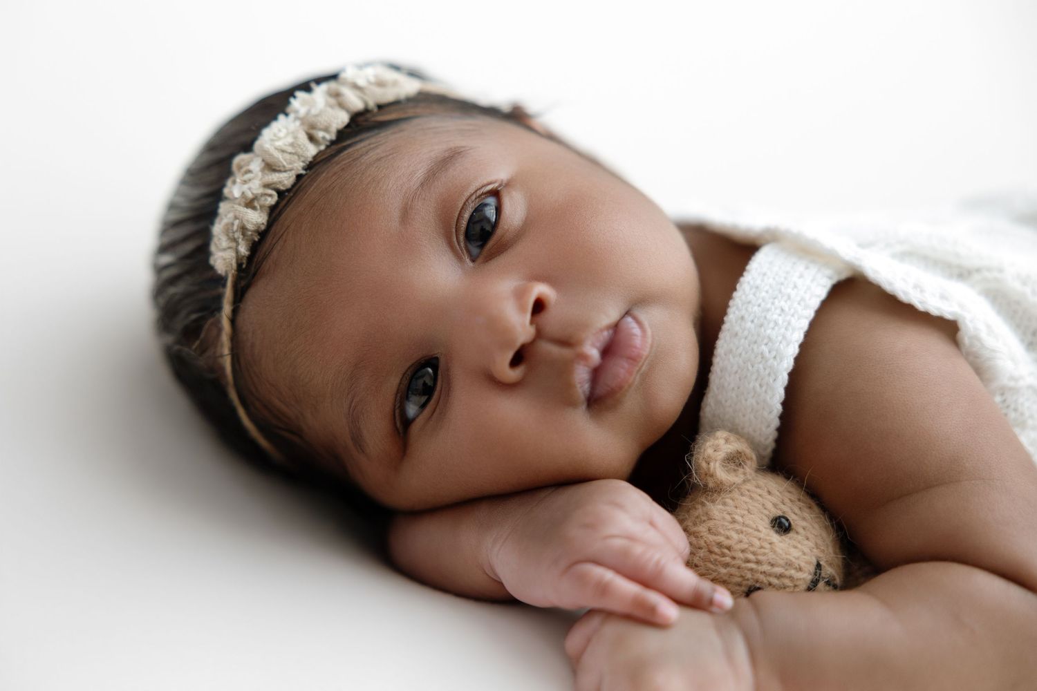 Sleeping newborn wrapped in soft pink swaddle on purple furry blanket with small decorative heart beside them.