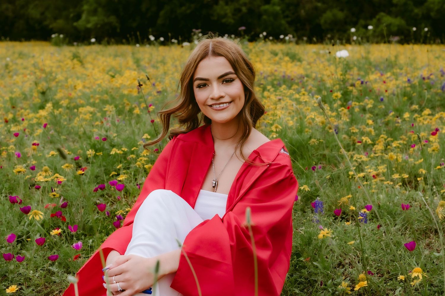 A person in a bright red jacket sits in a field of yellow wildflowers on a sunny day.