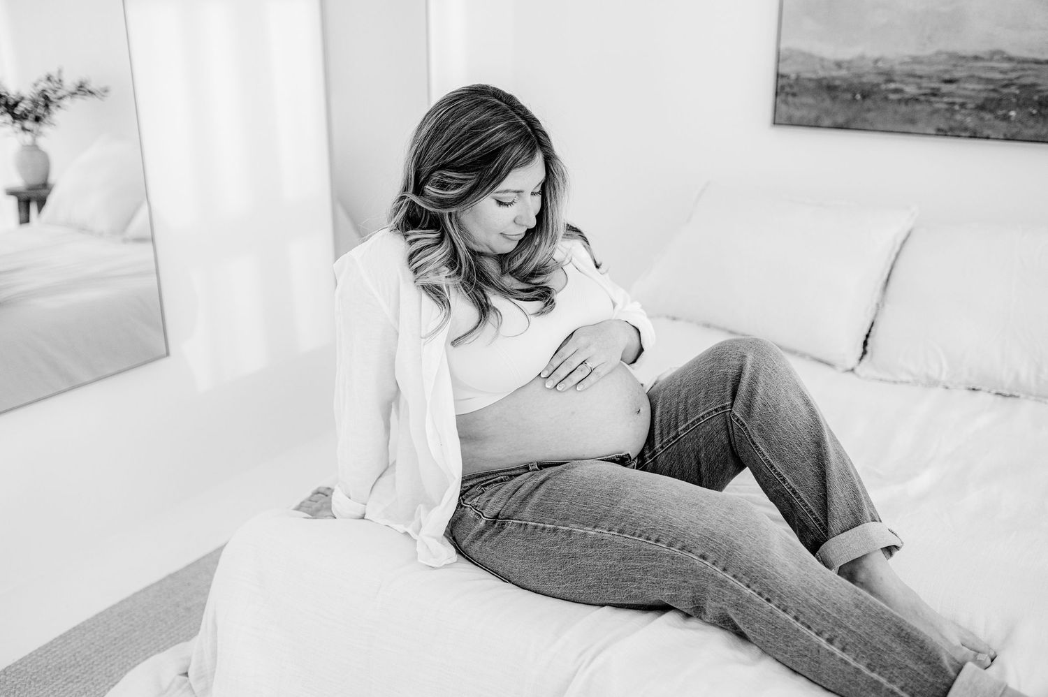 Jacksonville FL maternity photo in black and white shows a pregnant women relaxing in casual clothing on a  bed touching her belly.