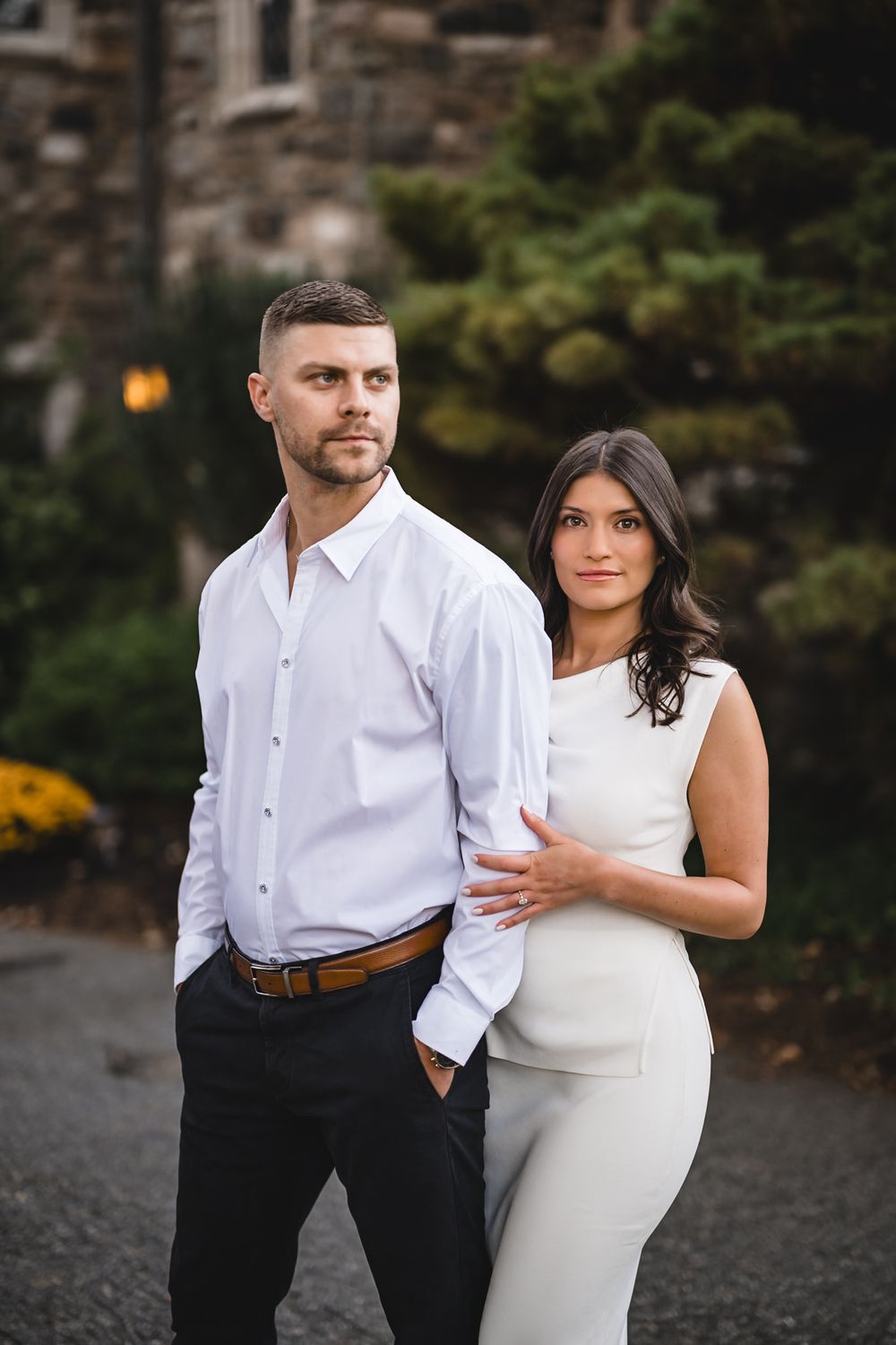 Couple in formal attire posing together against stone building backdrop.