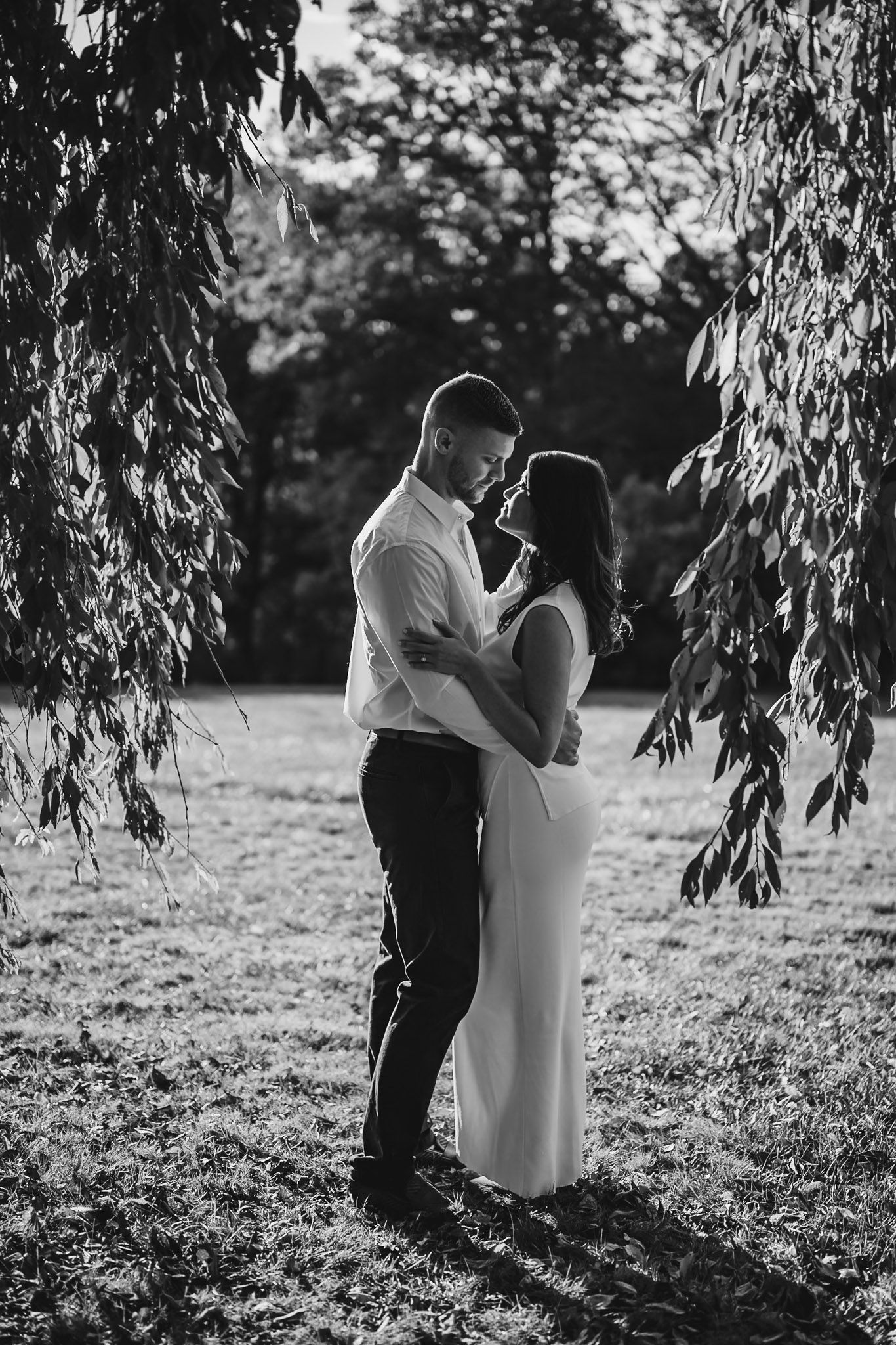 Black and white photo of a couple sharing an intimate moment under willow trees.