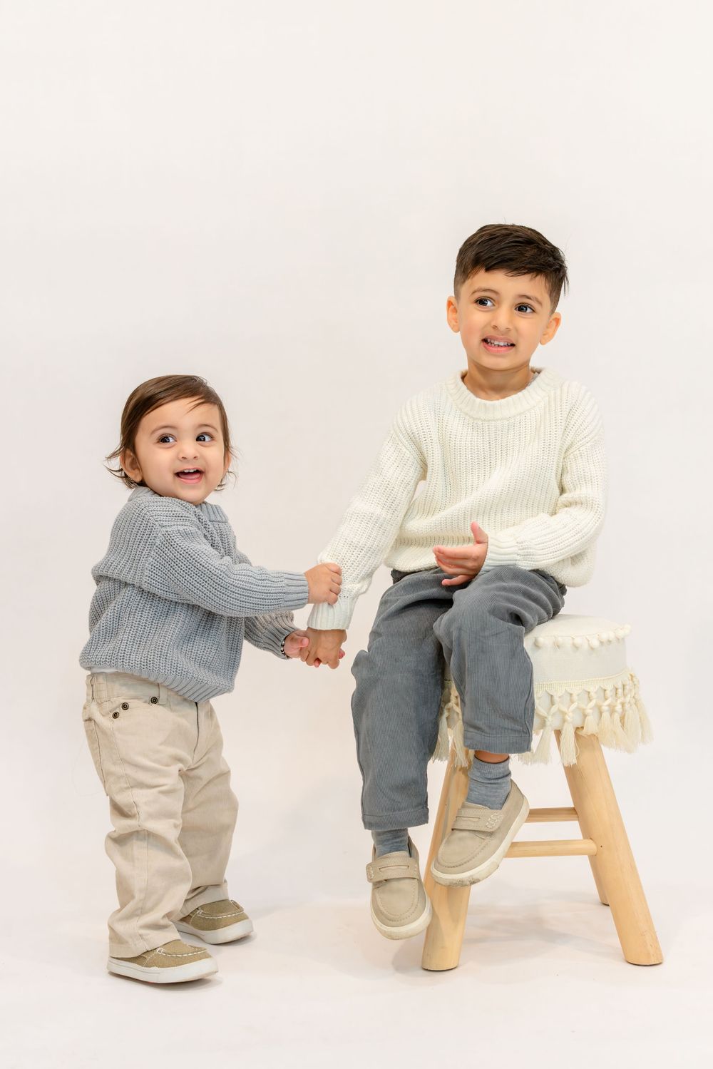 Three sequential photos show a toddler in a gray sweater and khaki pants playfully interacting with a wooden stool.