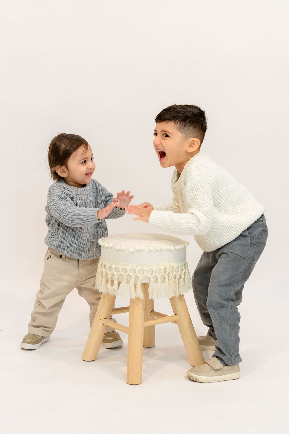 Two children playfully interact around a white macrame stool in a progressive sequence of photos.