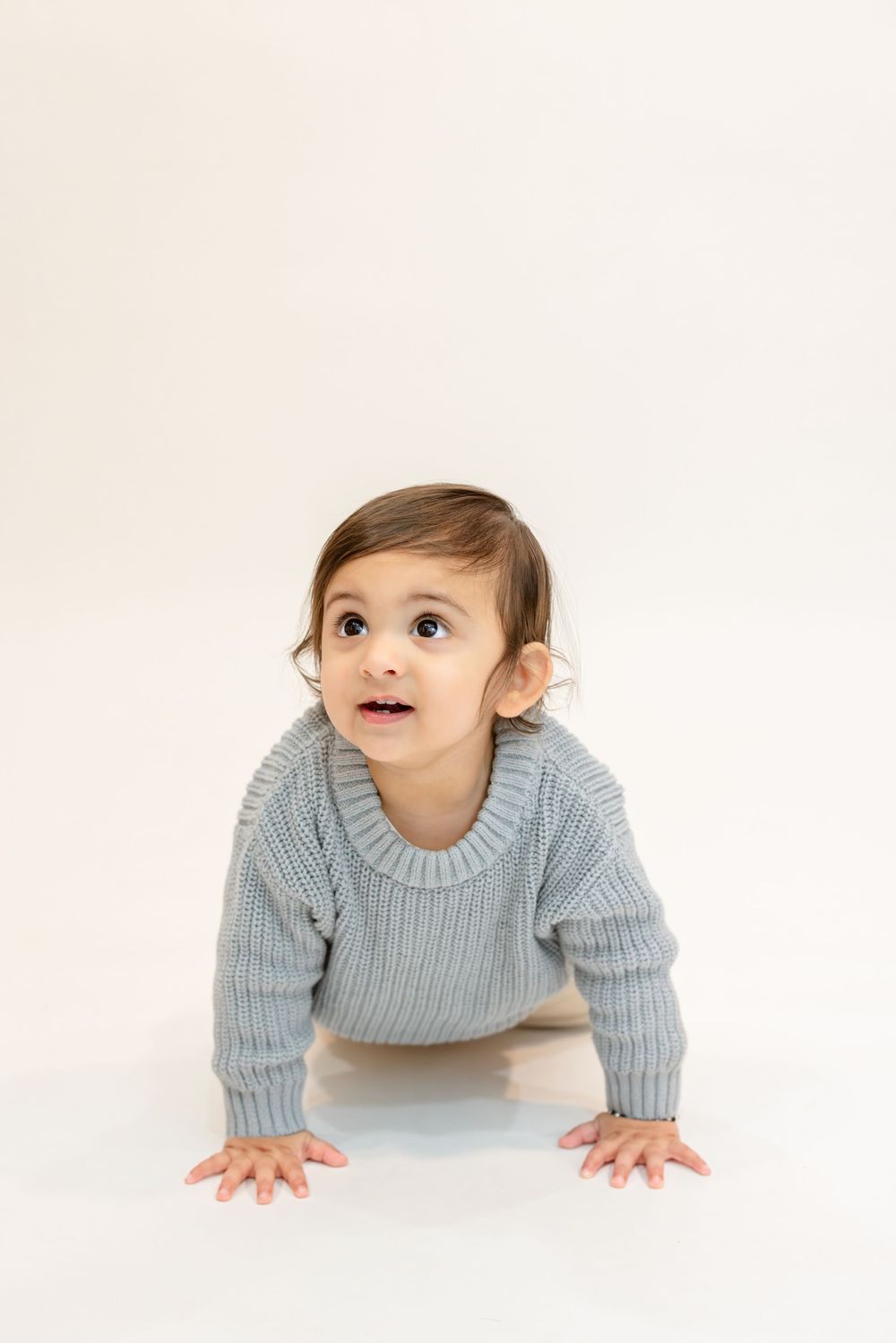 A baby in a light blue sweater crawls on a white background in a three-photo sequence.