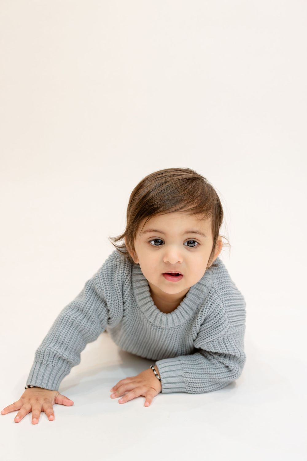 Baby in gray knit sweater lying on white background in three different poses.