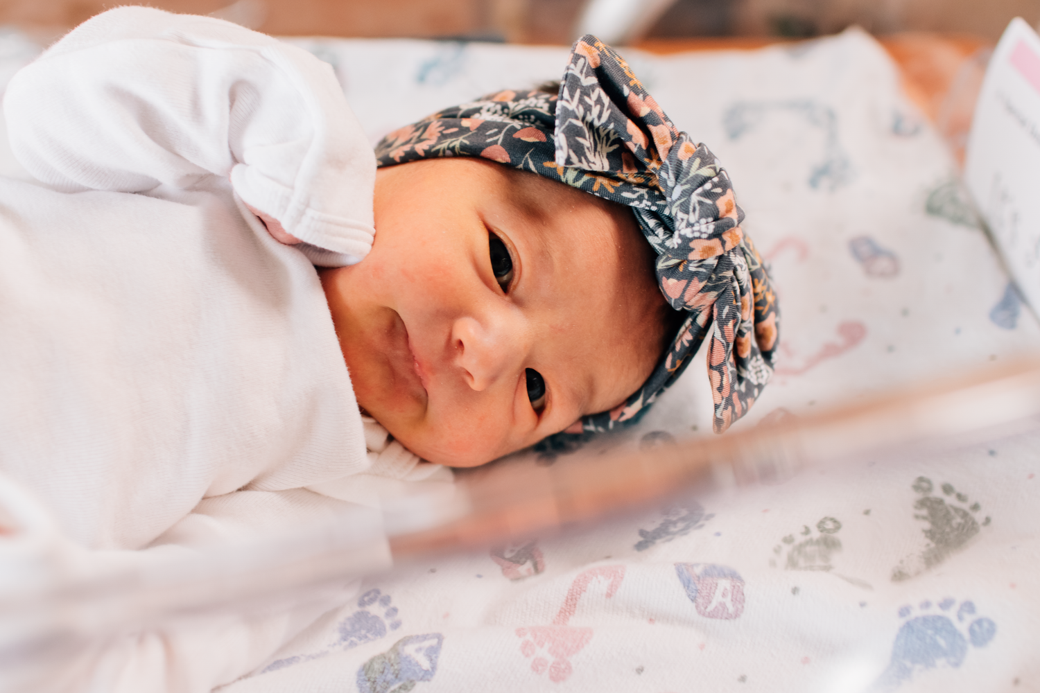 A sleeping baby wearing a floral headband lies peacefully on white bedding.