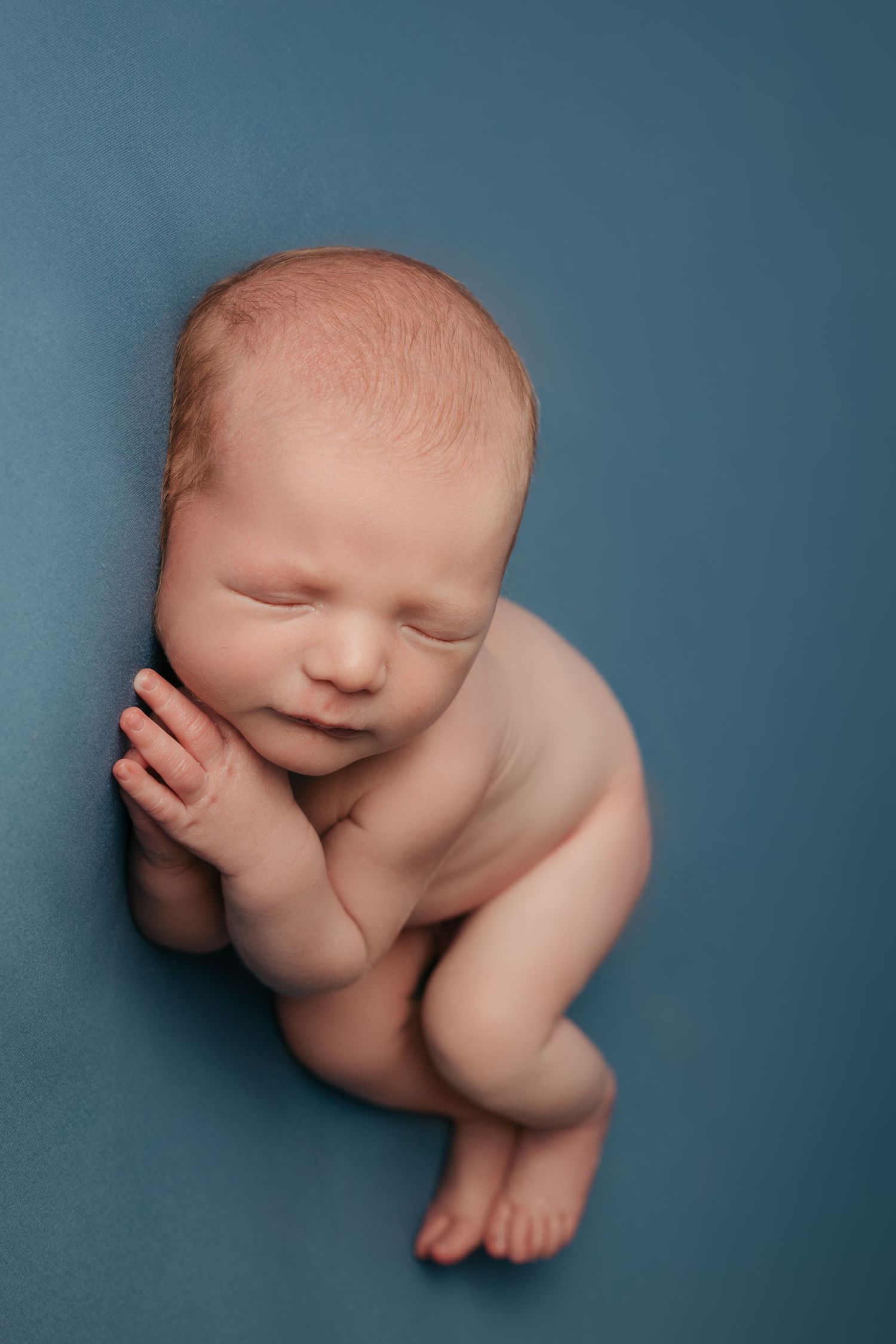 Artistic newborn photography poses on blue backdrop showing curled up sleeping baby.