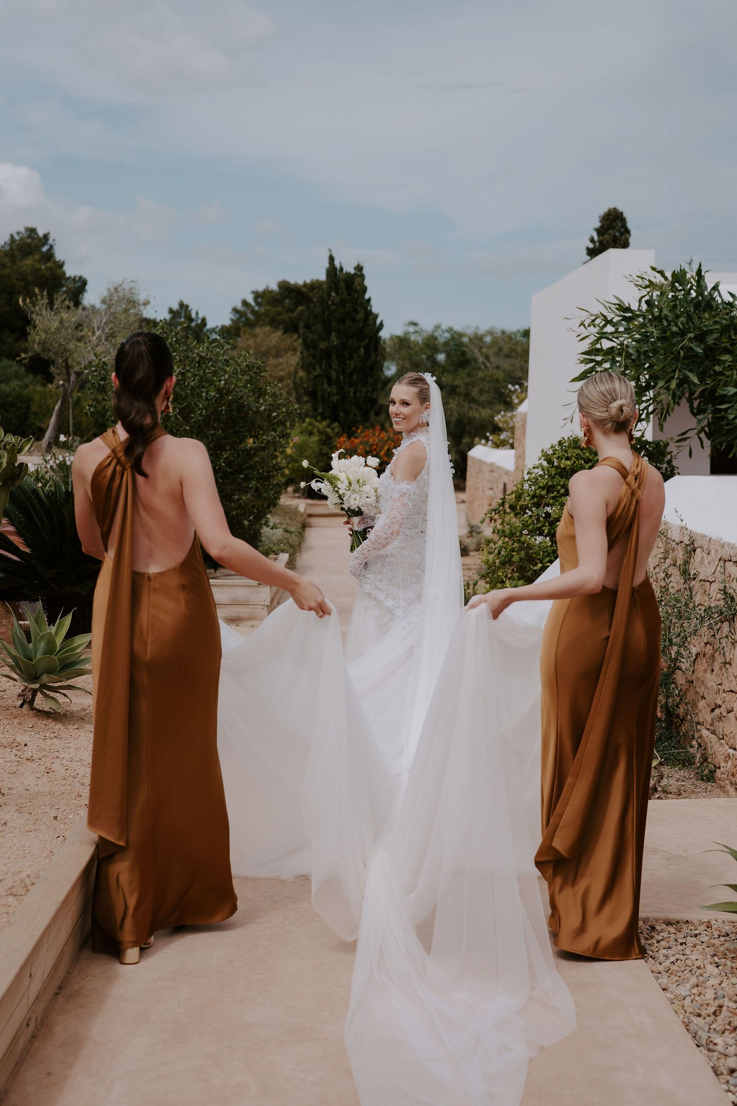 bride looking over shoulder smiling as bridesmaids carry her dress