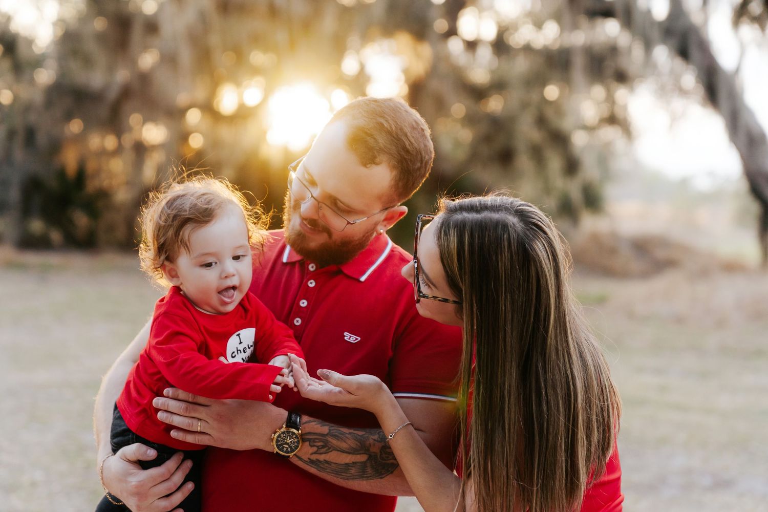 A family in red outfits shares joyful moments together during an outdoor photo session at sunset.