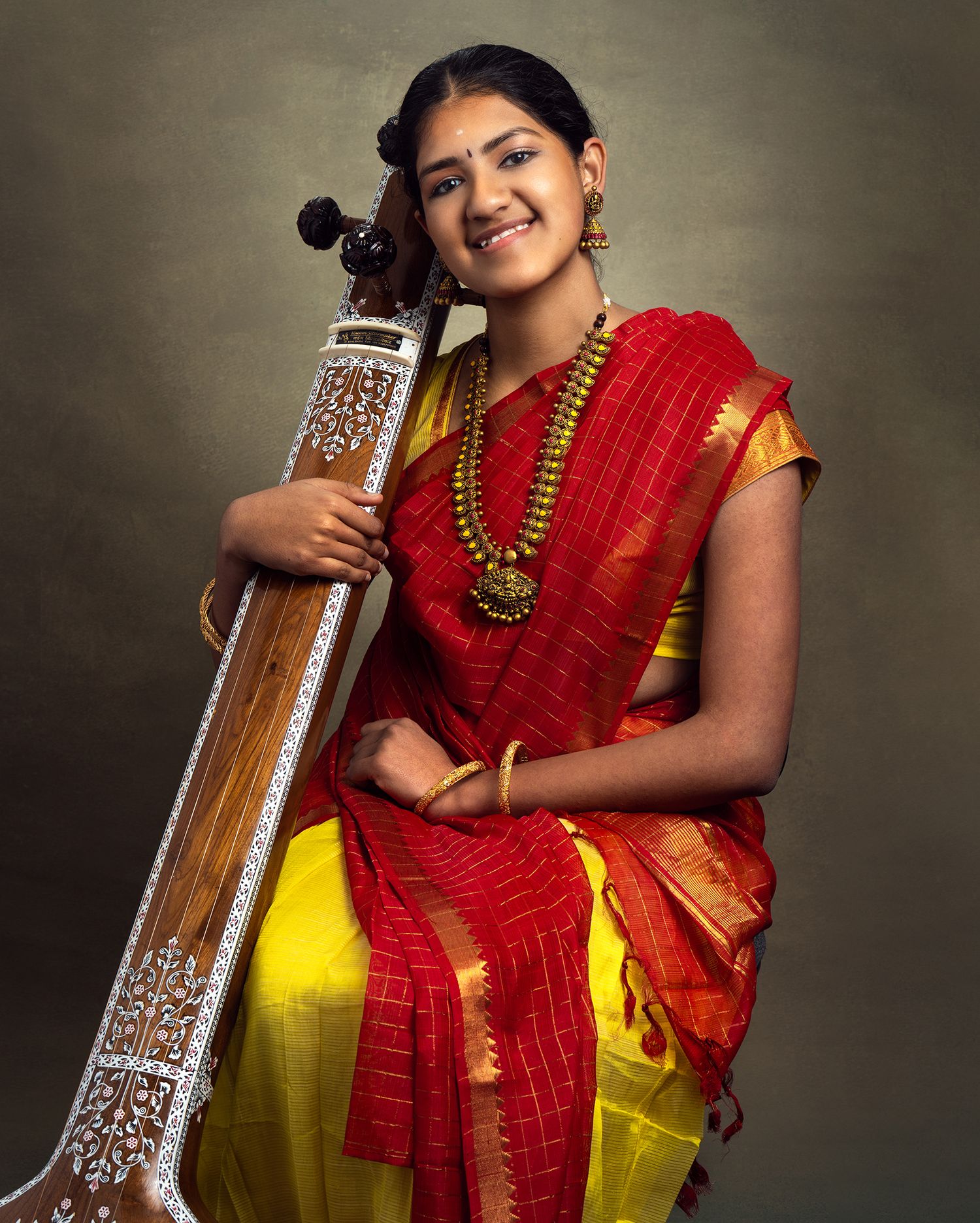Traditional Indian maternity photoshoot featuring a woman in red and yellow saree with temple jewelry.