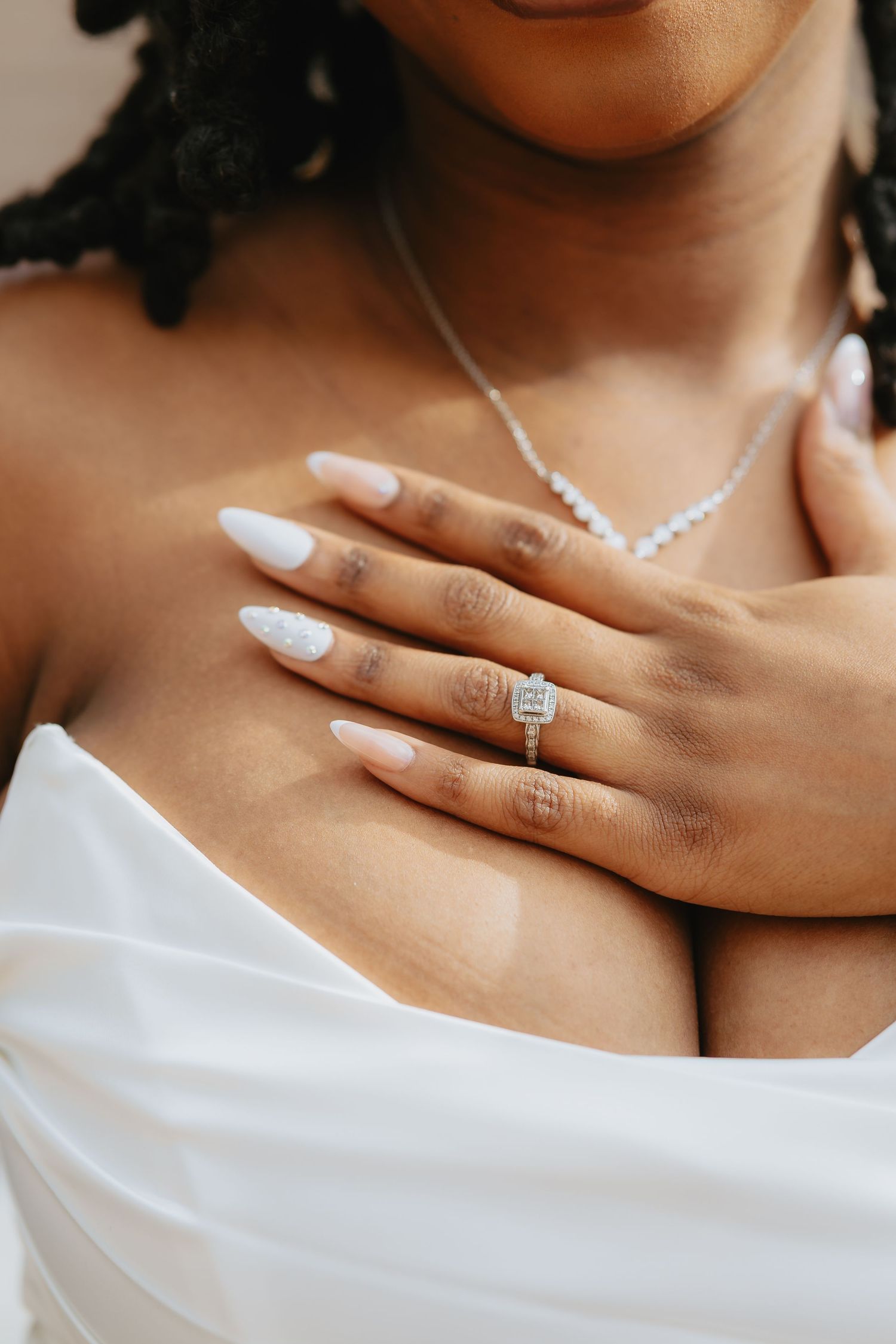 Close up shot of hands wearing a white diamond engagement ring against a white fabric background.