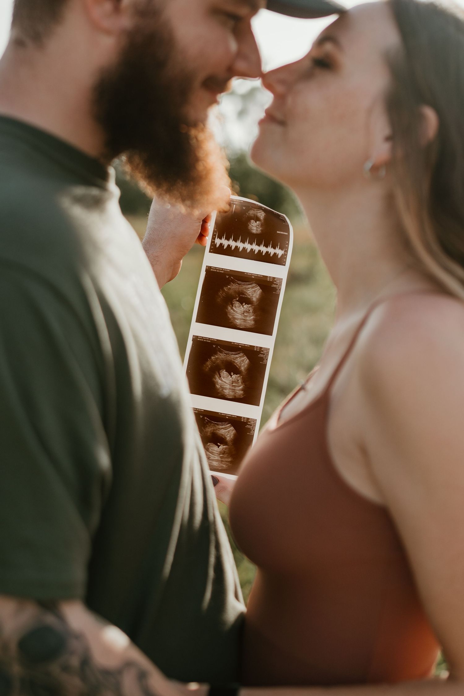 A couple holds up ultrasound photos during a romantic outdoor pregnancy announcement photoshoot at sunset.