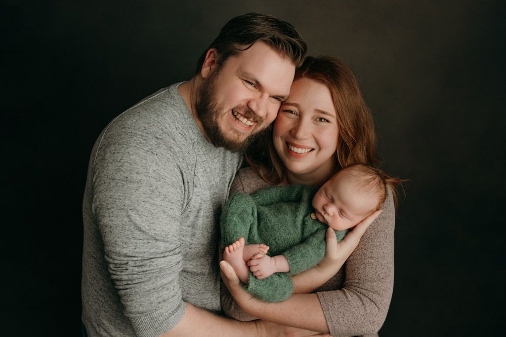 A couple embraces and smiles together holding their newborn baby during an intimate indoor photo session at the studio in victoria bc