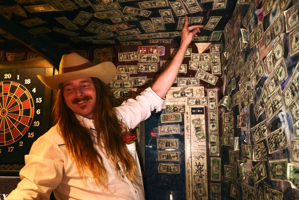 People celebrating under a ceiling decorated with dollar bills in a dimly lit bar on Broadway in Nashville