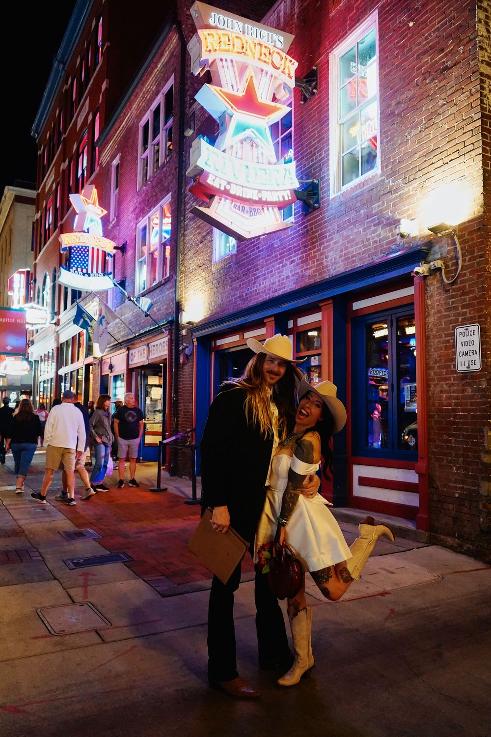 Neon signs illuminate a brick building facade on a city street at night.