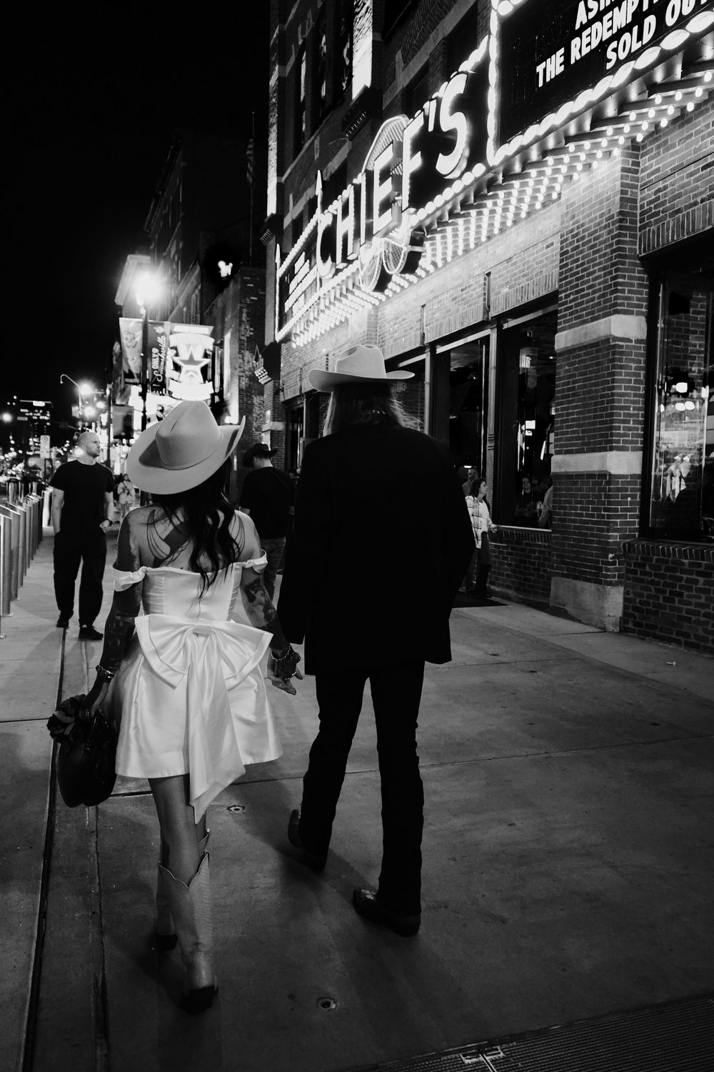 People walking down a city street at night in black and white. Couple on Broadway in Nashville.