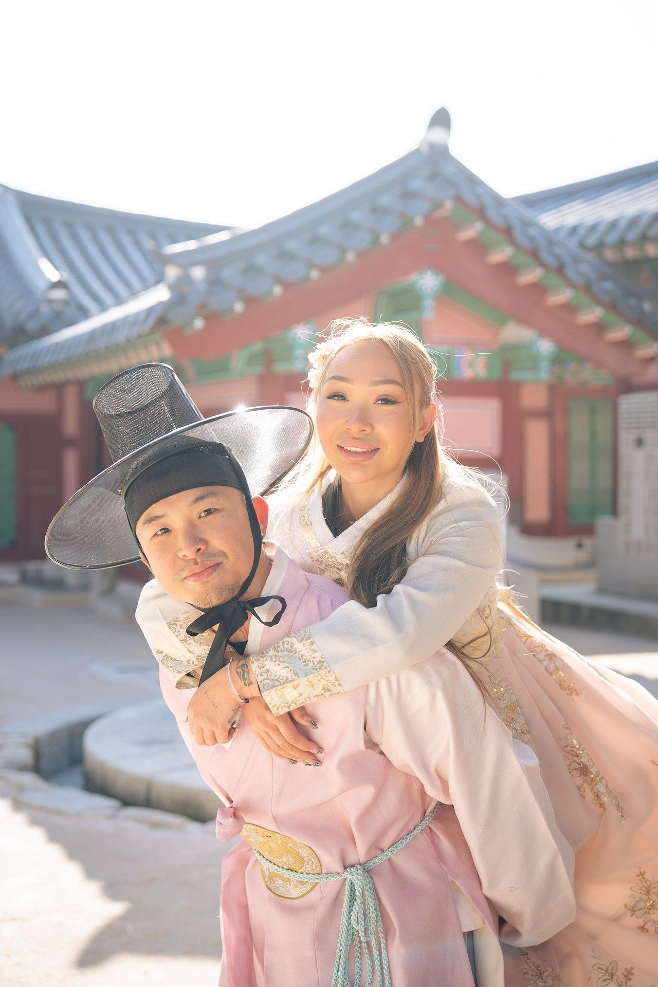 People in traditional Korean hanbok clothing pose playfully at a historic palace courtyard on a sunny day.