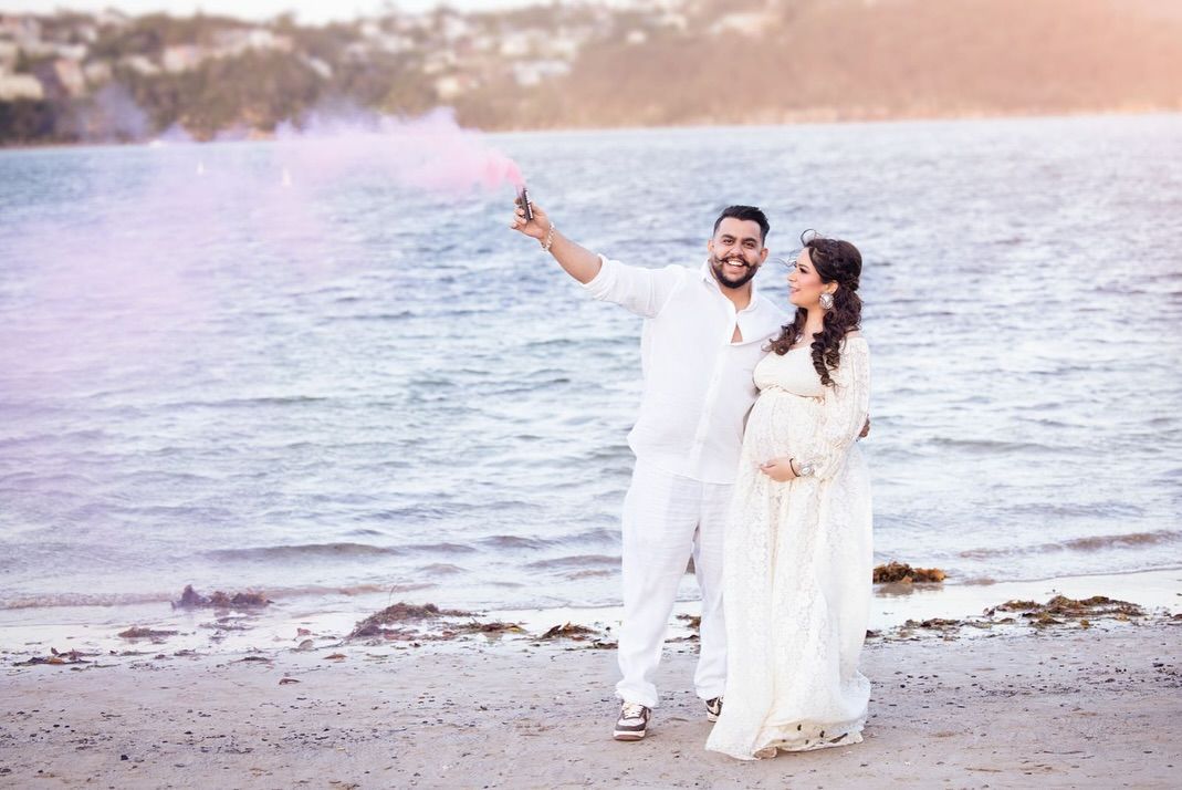 Couple in white outfits walking along a beach at sunset, holding hands and enjoying a romantic moment by the ocean.