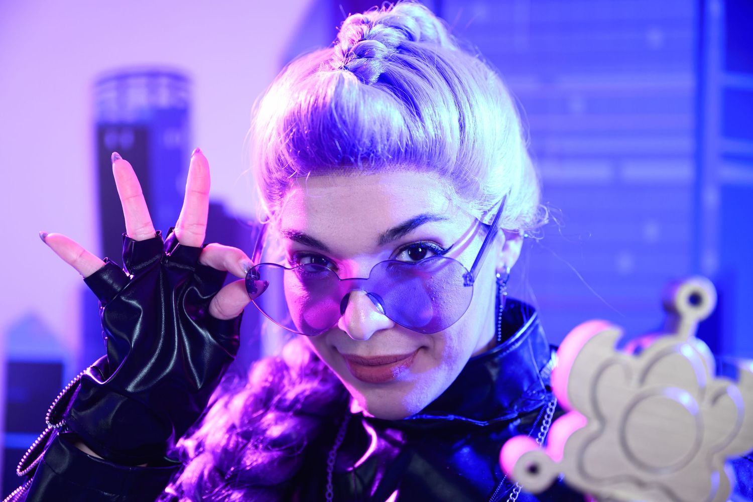 A performer in dramatic purple lighting holds up their hand while wearing dark gloves and dramatic makeup.
