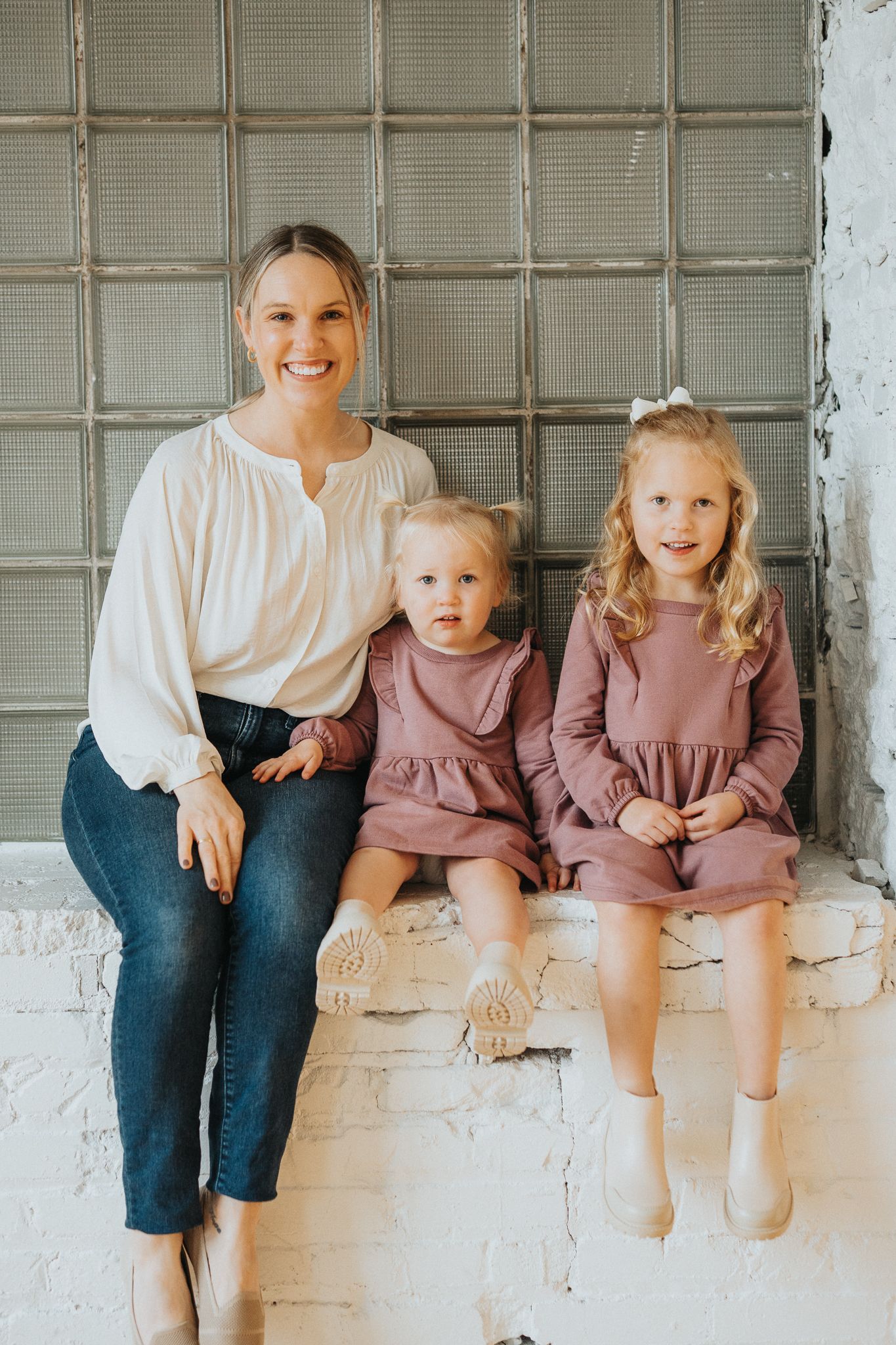 A group sits together on a white windowsill wearing coordinated outfits of jeans and dusty pink dresses.