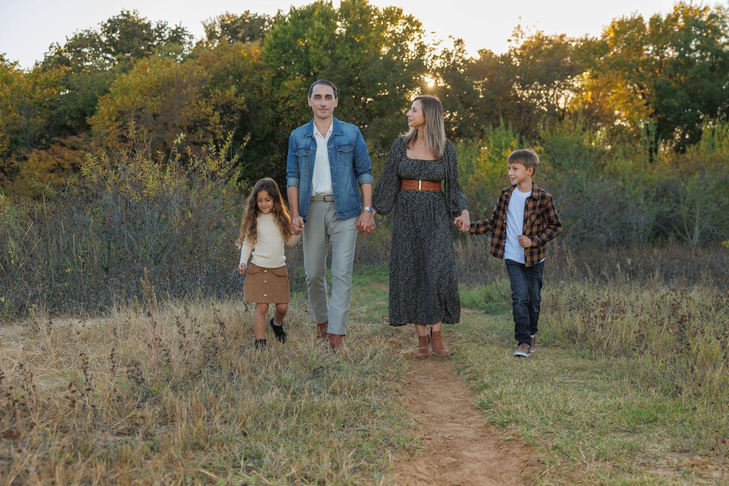 A group of people walking together on a dirt path through a golden meadow at sunset.