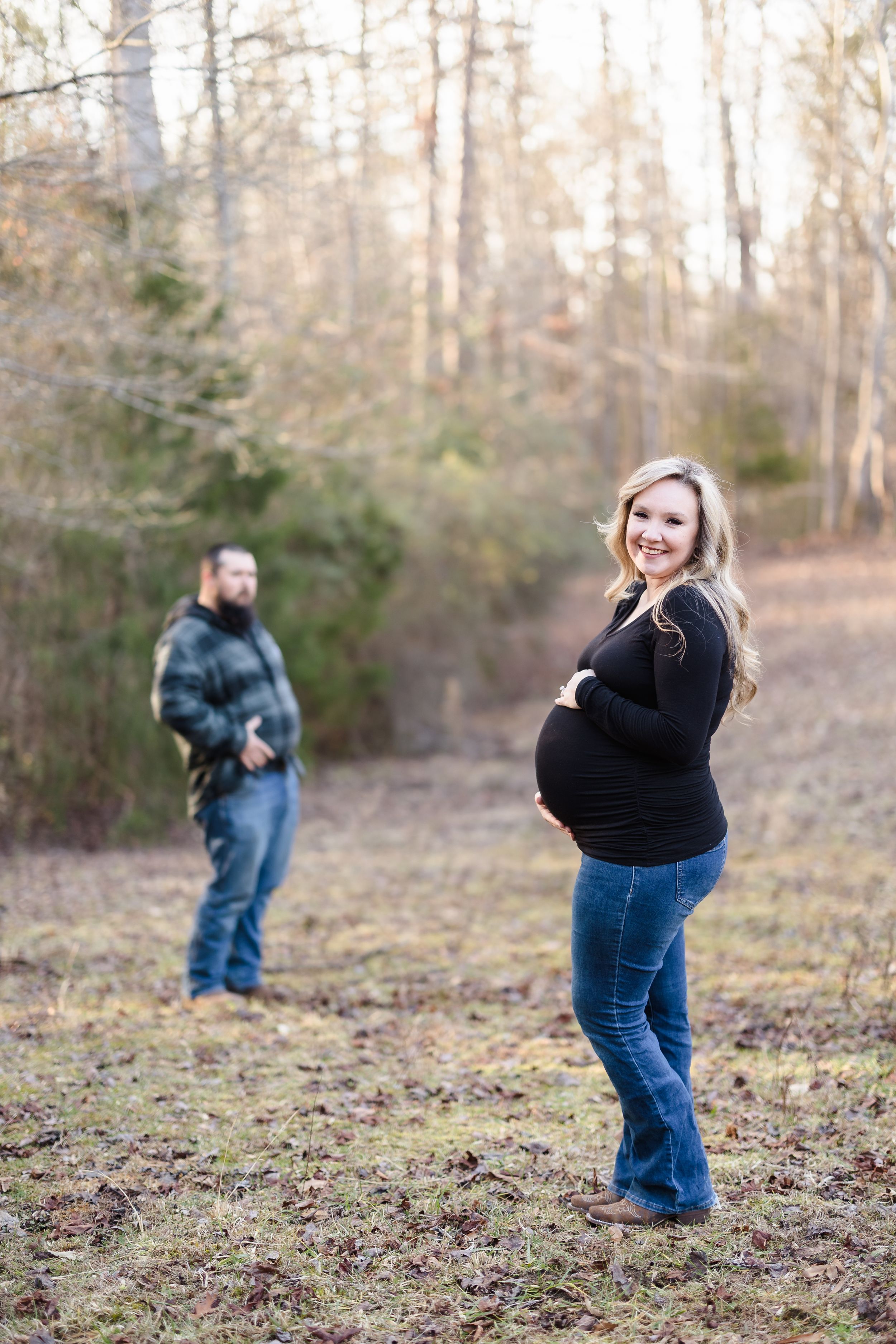 Maternity photo in wooded setting with couple in casual attire.