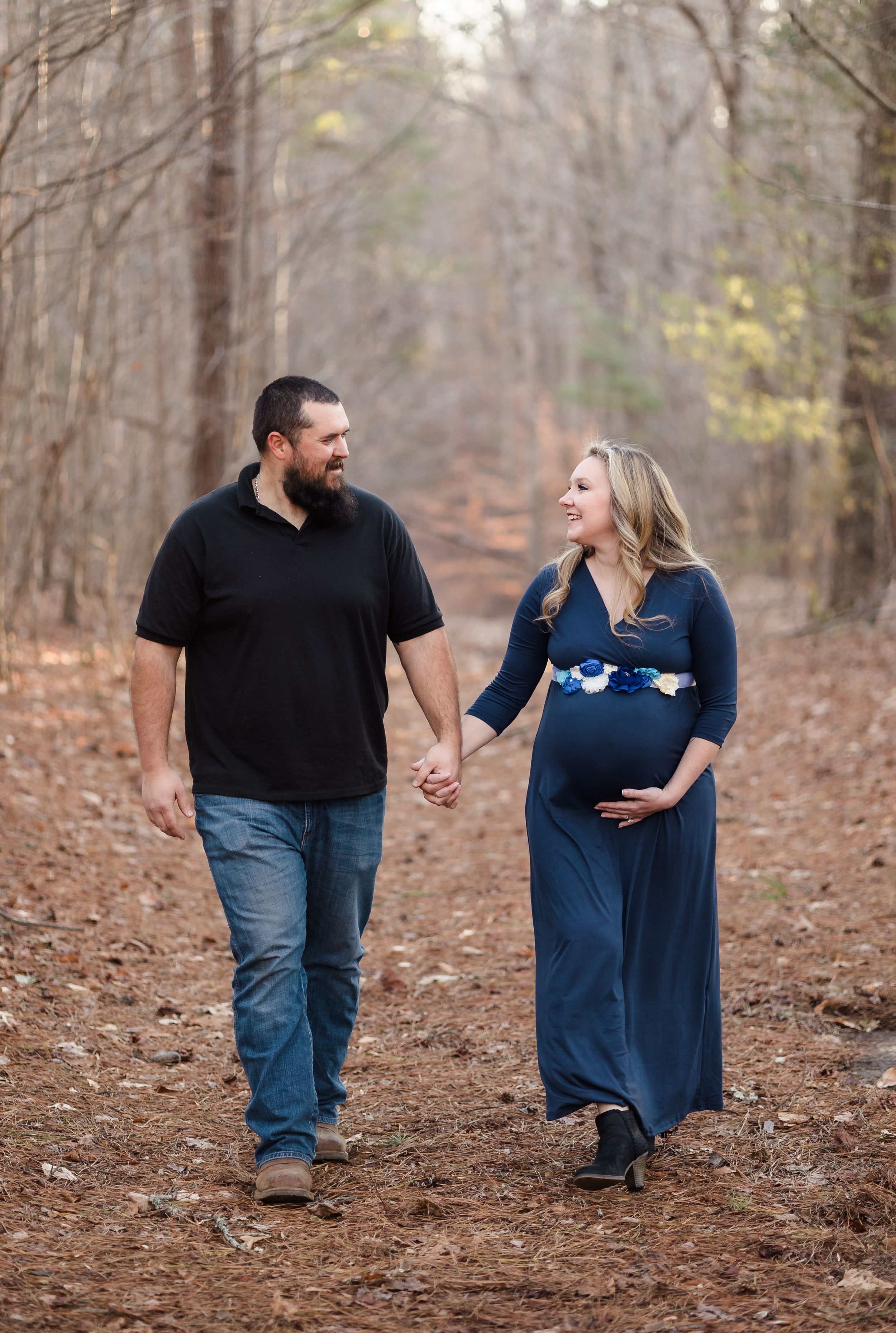 Expecting couple walking hand in hand on forest trail during maternity photoshoot.