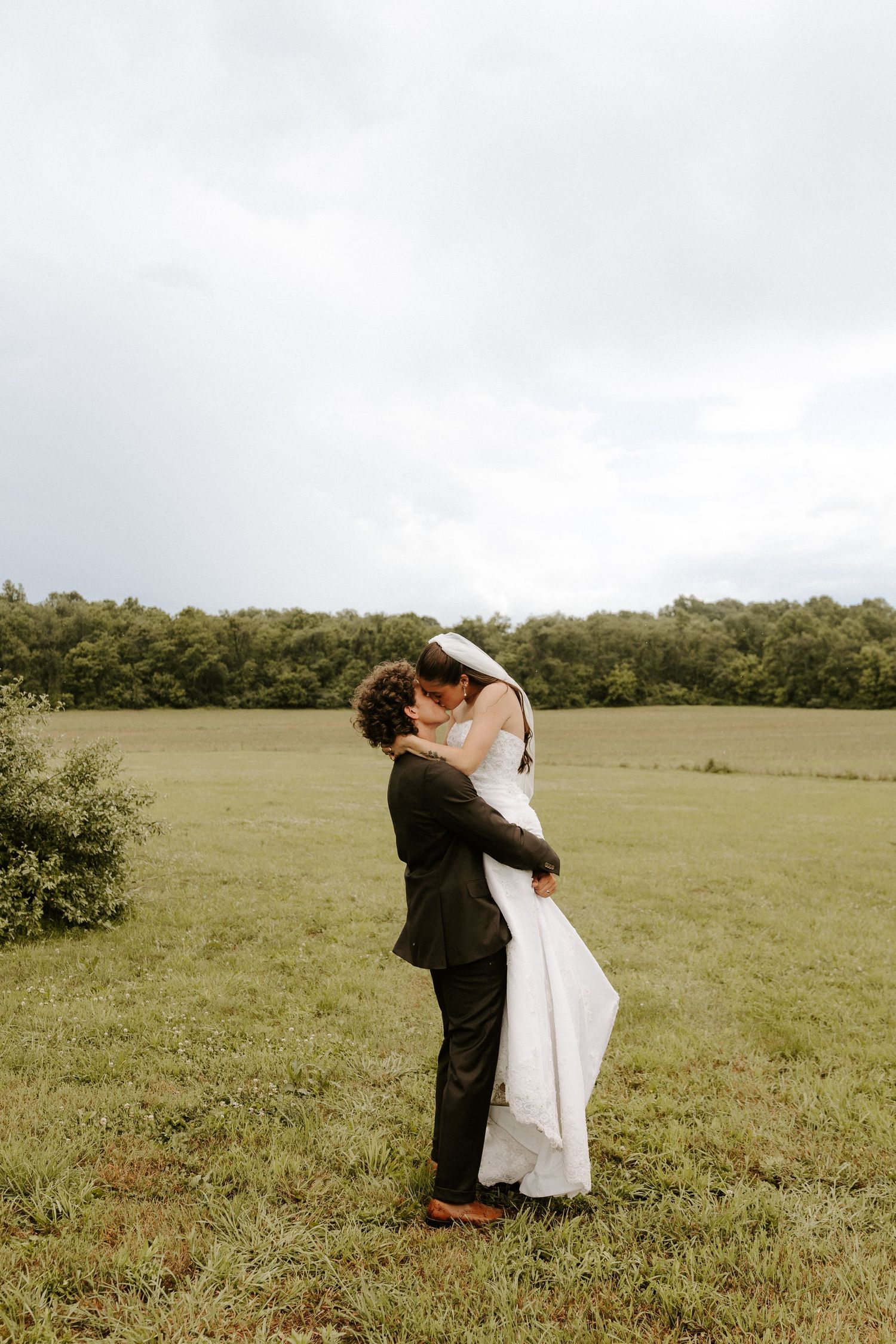 Groom dips bride for a kiss on a brick pathway outside a historic red building.