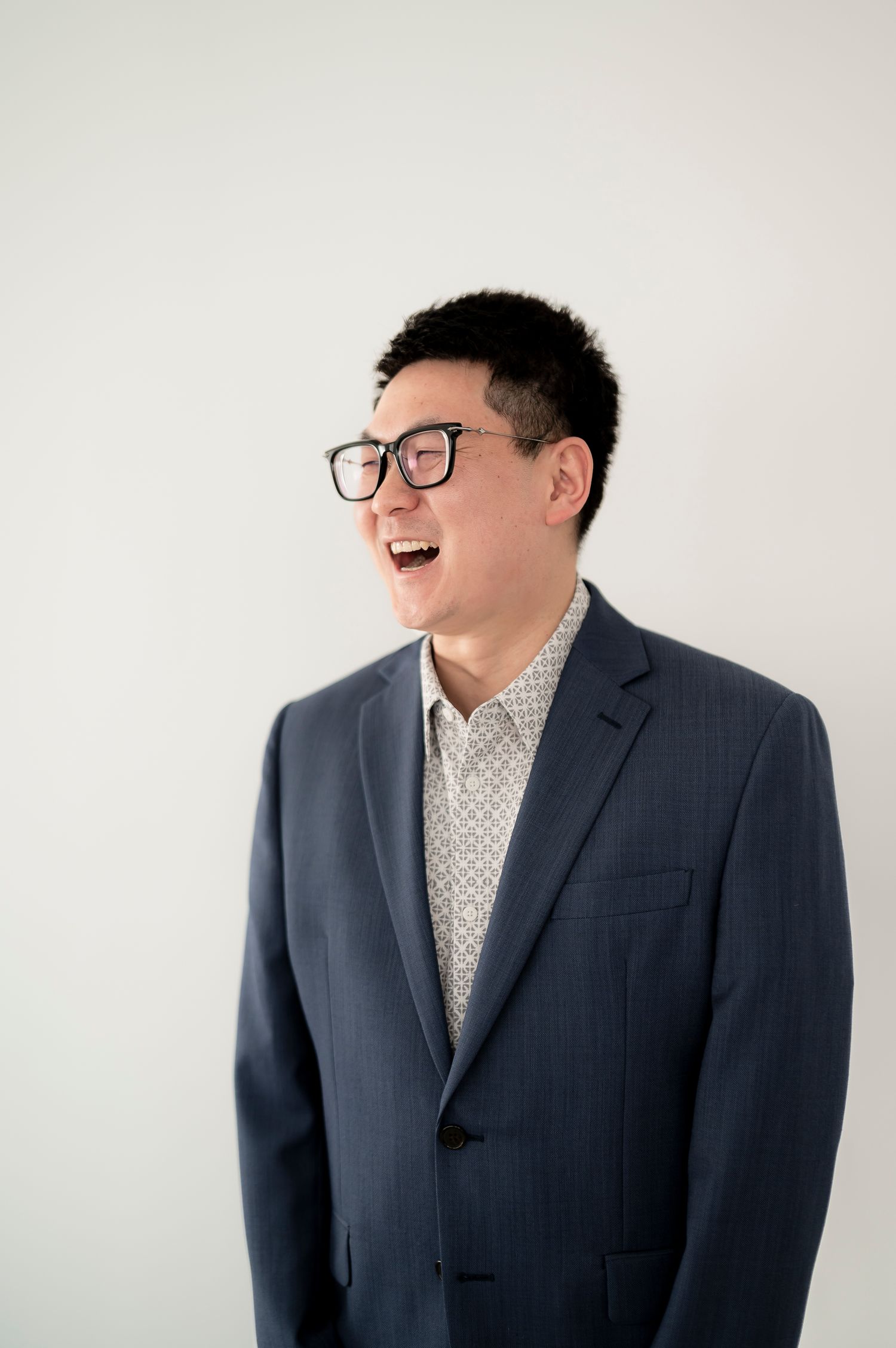 Professional wearing a grey suit and polka dot shirt laughs joyfully against a white background in a photo series.