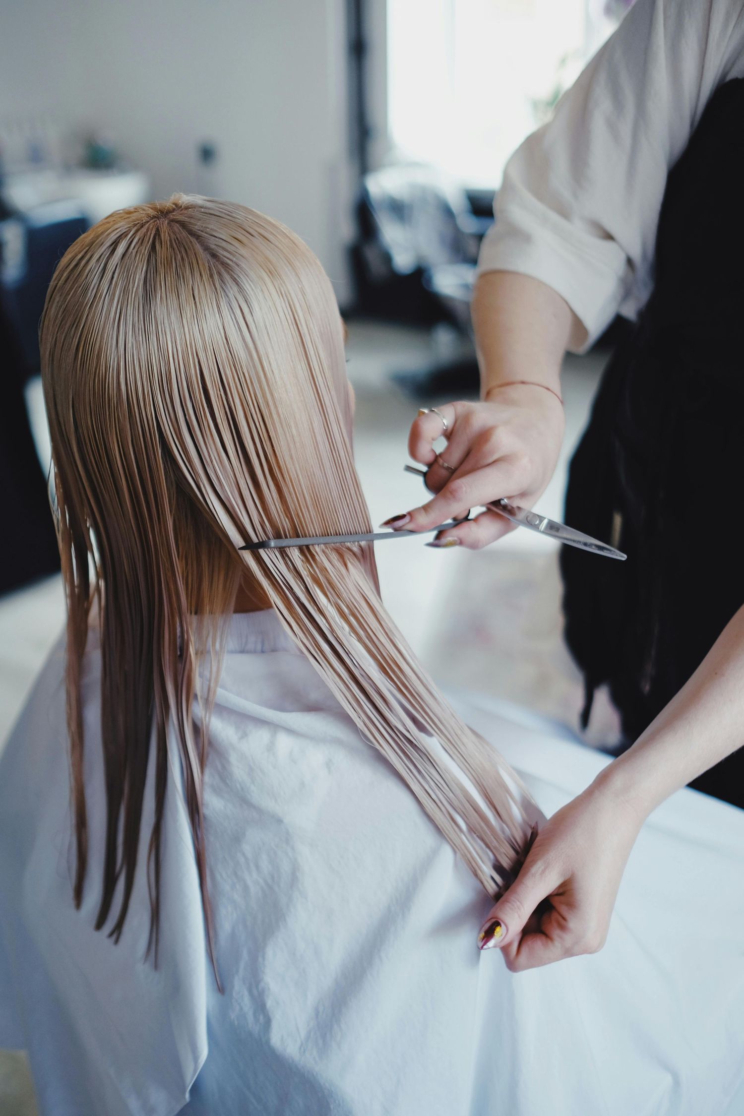 Professional hairdresser demonstrates step by step haircut technique on blonde hair in salon setting.