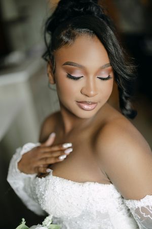 Elegant bride with glam makeup and updo hairstyle wearing an off-shoulder lace wedding gown.
