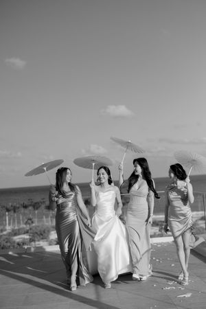 A group in formal attire holding parasols poses together on a sunny beach for a wedding photo shoot.