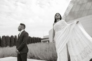 Black and white photo of couple standing apart dramatically with tall grass and pyramid building behind.