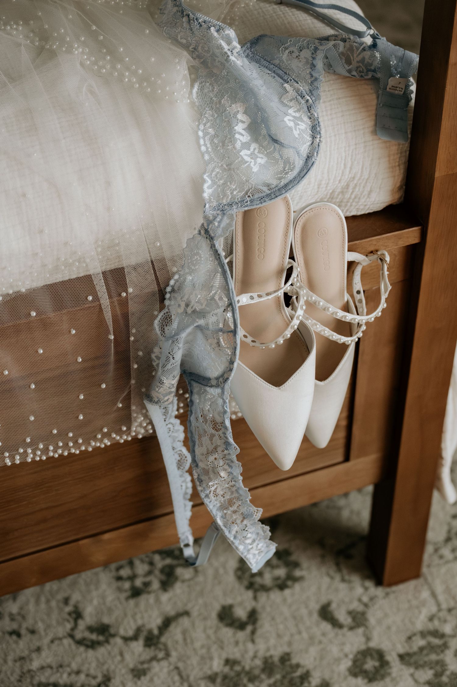 White bridal shoes and delicate veil displayed on wooden shelf.