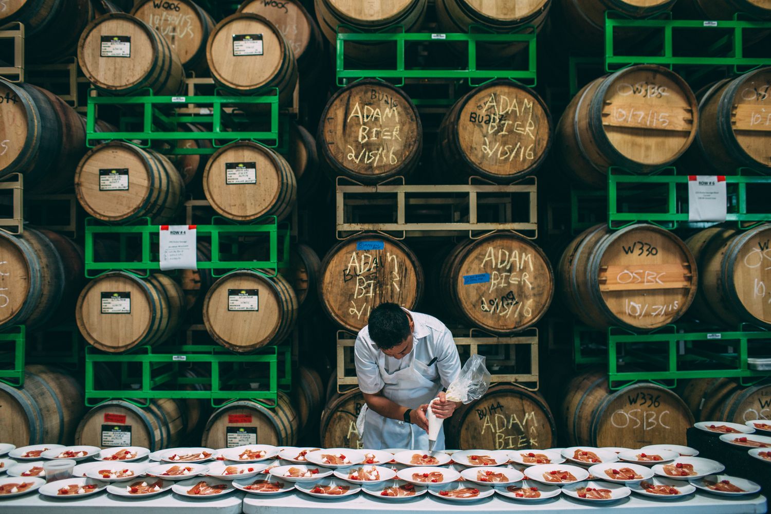 Wooden whiskey barrels stacked in rows on green metal racks in a distillery warehouse.