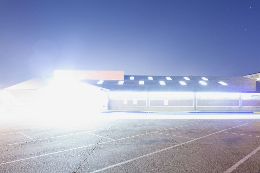 Empty parking lot with bright overhead lights casting shadows at dusk.