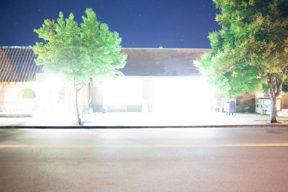 Commercial buildings with green trees lit up at night under clear sky.