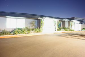 Long empty concrete driveway leading to commercial buildings under blue sky.